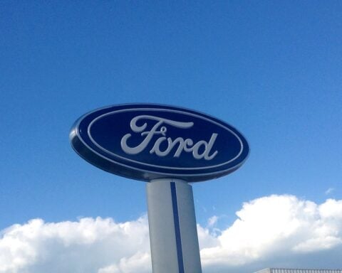 A tall Ford logo sign mounted on a pillar against a bright blue sky.