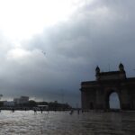 Gateway of India in Mumbai during monsoon season with cloudy skies and wet ground.