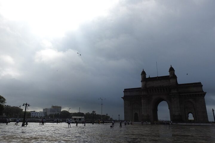 Gateway of India in Mumbai during monsoon season with cloudy skies and wet ground.
