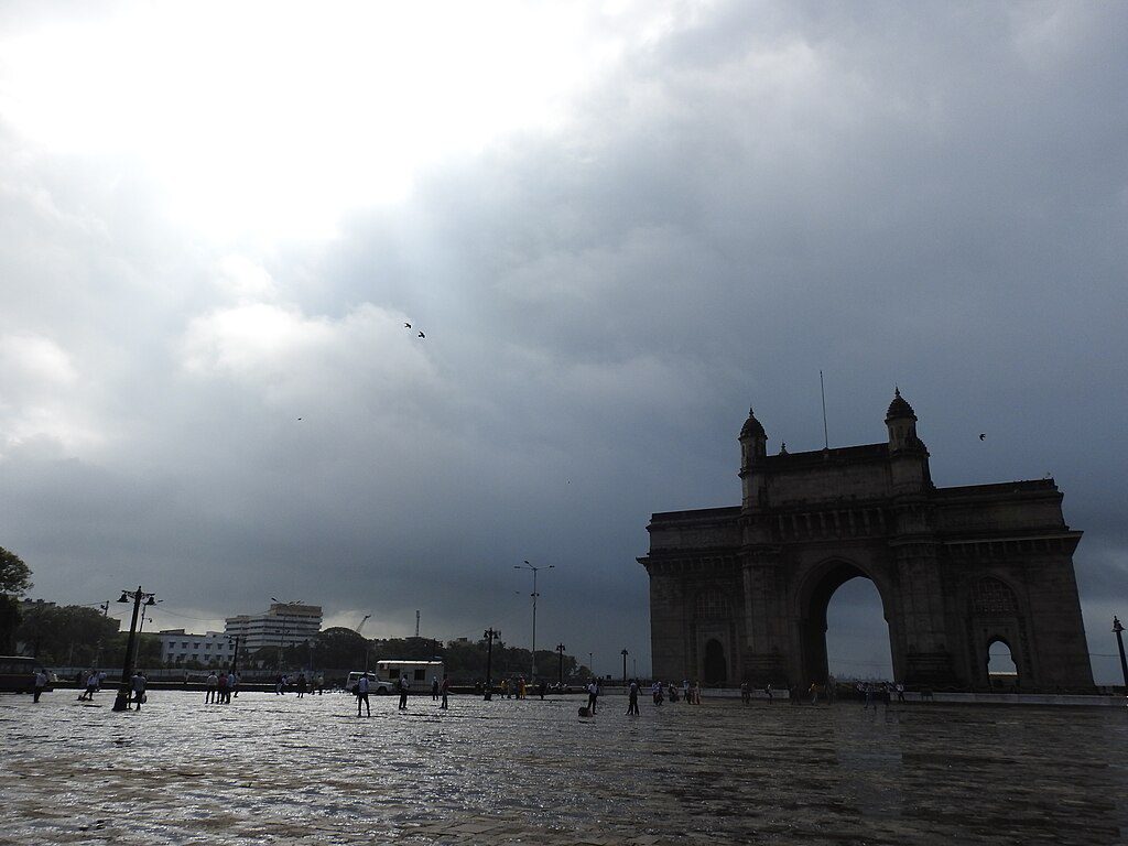 Gateway of India in Mumbai during monsoon season with cloudy skies and wet ground.