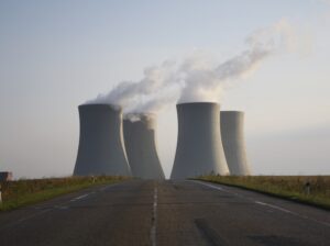 Nuclear power plant with four cooling towers emitting steam against a misty background, viewed from an empty road leading toward the facility.