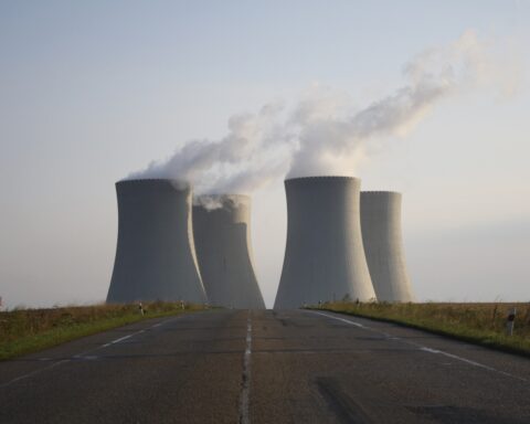 Nuclear power plant with four cooling towers emitting steam against a misty background, viewed from an empty road leading toward the facility.