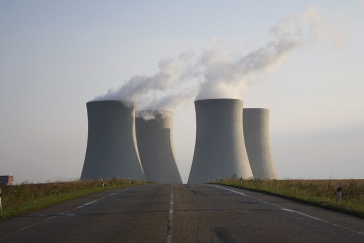 Nuclear power plant with four cooling towers emitting steam against a misty background, viewed from an empty road leading toward the facility.