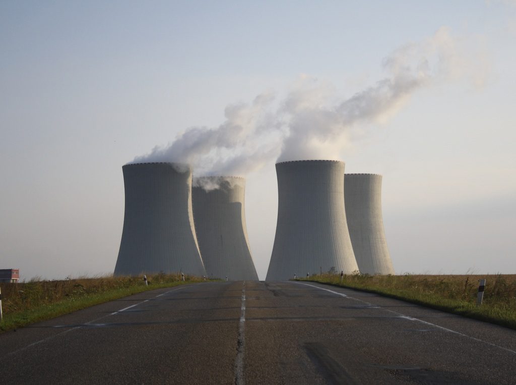 Nuclear power plant with four cooling towers emitting steam against a misty background, viewed from an empty road leading toward the facility.