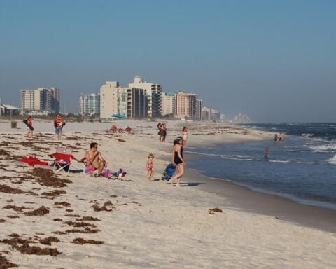Families on Orange Beach, Alabama, with waves and condos along the Gulf Coast shoreline on a sunny day.