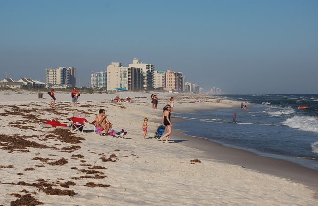Families on Orange Beach, Alabama, with waves and condos along the Gulf Coast shoreline on a sunny day.