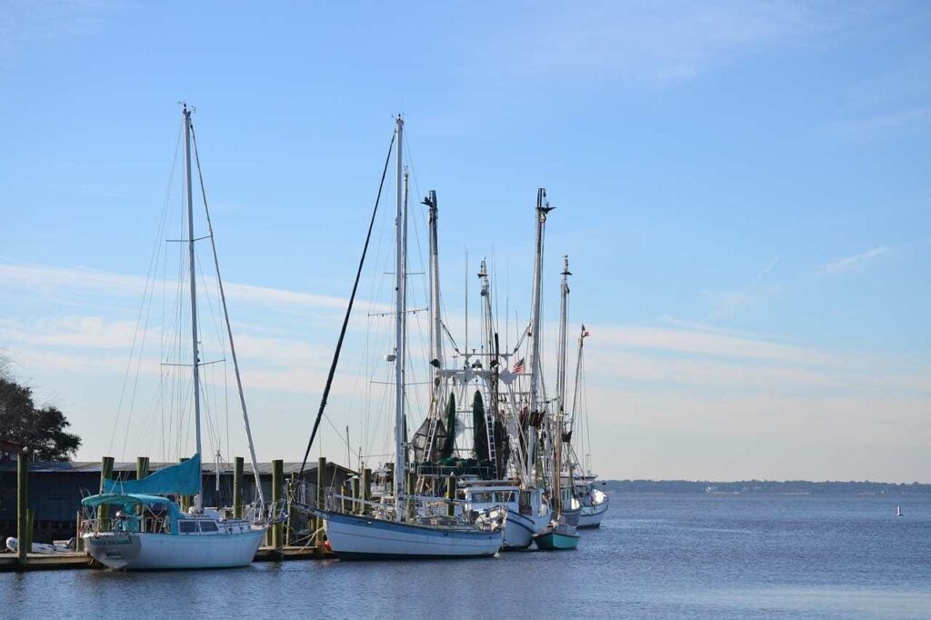 Several commercial fishing boats and vessels with tall masts docked at Shem Creek harbor on a clear day with blue skies, representing the type of commercial fishing fleet impacted by the Hawaii federal court ruling.