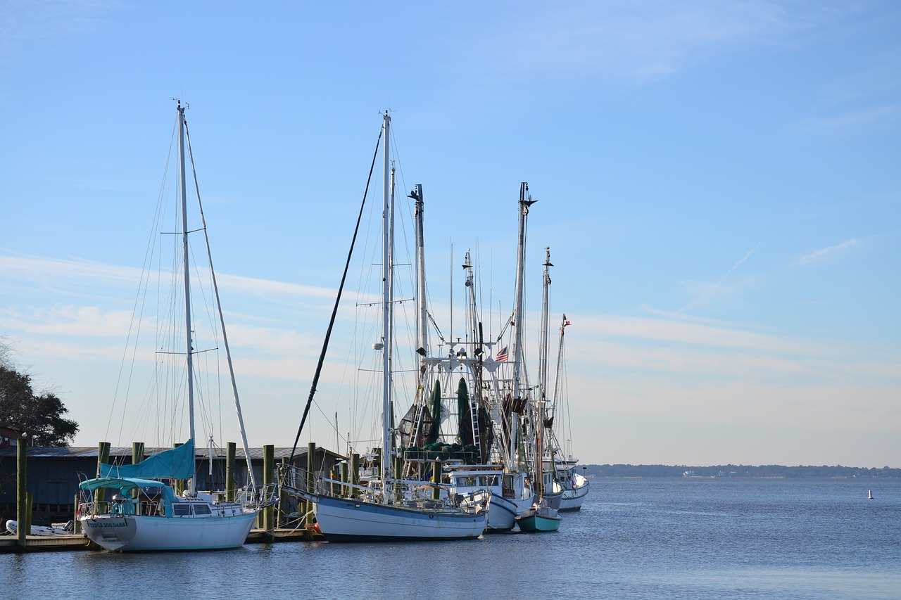 Several commercial fishing boats and vessels with tall masts docked at Shem Creek harbor on a clear day with blue skies, representing the type of commercial fishing fleet impacted by the Hawaii federal court ruling.