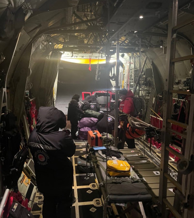 Medics and support personnel secure stretchers and equipment inside the open rear of a Hercules on an ice runway.