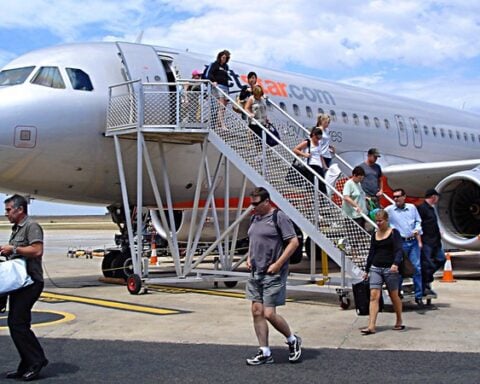Passengers walking down aircraft stairs from Jetstar Airbus A320-200 plane at Avalon Airport with ground crew and luggage handling visible on tarmac