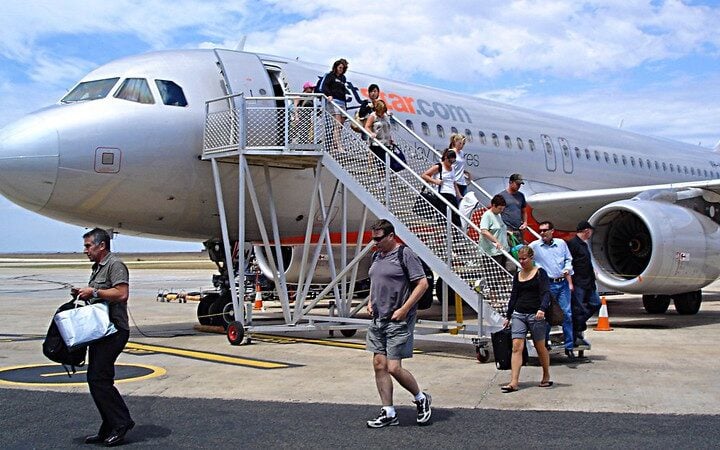 Passengers walking down aircraft stairs from Jetstar Airbus A320-200 plane at Avalon Airport with ground crew and luggage handling visible on tarmac