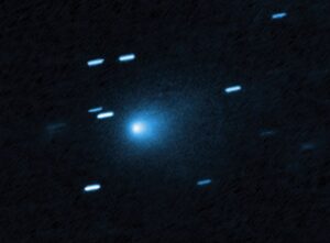 Hubble Space Telescope image of interstellar comet 3I/ATLAS showing a bright blue-white nucleus surrounded by a diffuse teardrop-shaped coma against a dark background with streaked stars appearing as short blue lines due to the telescope tracking the fast-moving comet.