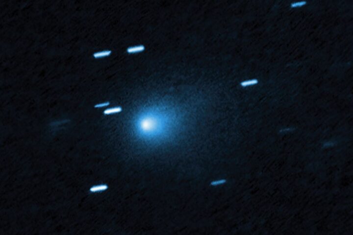 Hubble Space Telescope image of interstellar comet 3I/ATLAS showing a bright blue-white nucleus surrounded by a diffuse teardrop-shaped coma against a dark background with streaked stars appearing as short blue lines due to the telescope tracking the fast-moving comet.