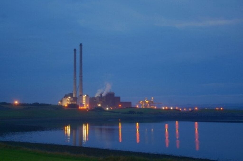Evening view of ESB Moneypoint Power Station on the Shannon Estuary, twin stacks lit against a deep blue sky with lights reflecting on calm water, County Clare.
