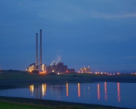 Evening view of ESB Moneypoint Power Station on the Shannon Estuary, twin stacks lit against a deep blue sky with lights reflecting on calm water, County Clare.