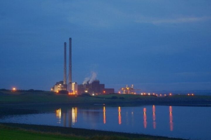 Evening view of ESB Moneypoint Power Station on the Shannon Estuary, twin stacks lit against a deep blue sky with lights reflecting on calm water, County Clare.