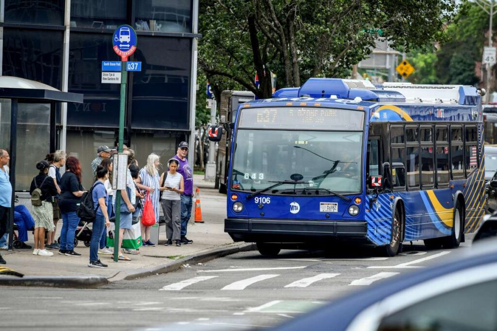 MTA Q31 Nova Bus approaches a Queens bus stop with riders waiting, illustrating the Queens Bus Network Redesign.