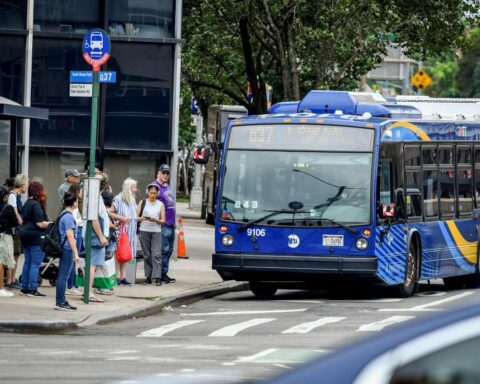 MTA Q31 Nova Bus approaches a Queens bus stop with riders waiting, illustrating the Queens Bus Network Redesign.