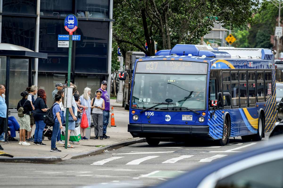MTA Q31 Nova Bus approaches a Queens bus stop with riders waiting, illustrating the Queens Bus Network Redesign.