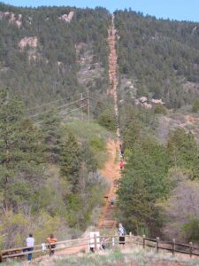 Hikers climbing the steep, wooden railroad-tie steps of the Manitou Incline through a densely forested mountainside.