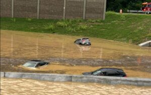 Flooded interstate with stalled vehicles and emergency lights visible in the distance. Photo Source: @JCGroves (X formerly Twitter)
