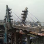 Cable-stayed metro bridge under construction over Mumbai’s Western Express Highway in 2013, with blue stay cables, pylons, scaffolding, workers on deck, and traffic below.