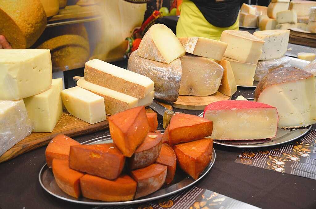 Representative Image. Assortment of various cheese types including soft cheese and orange-colored cheese displayed on a round metal serving platter.
