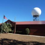 National Weather Service forecast office building with a NEXRAD Doppler radar dome at Mobile Regional Airport in Mobile, Alabama, under a clear blue sky.