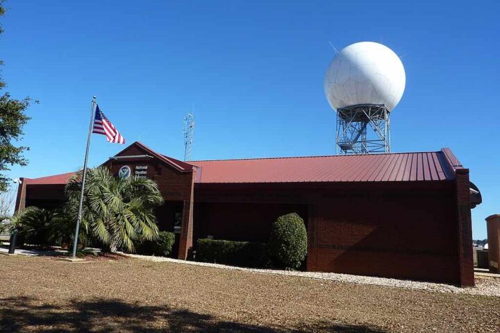 National Weather Service forecast office building with a NEXRAD Doppler radar dome at Mobile Regional Airport in Mobile, Alabama, under a clear blue sky.