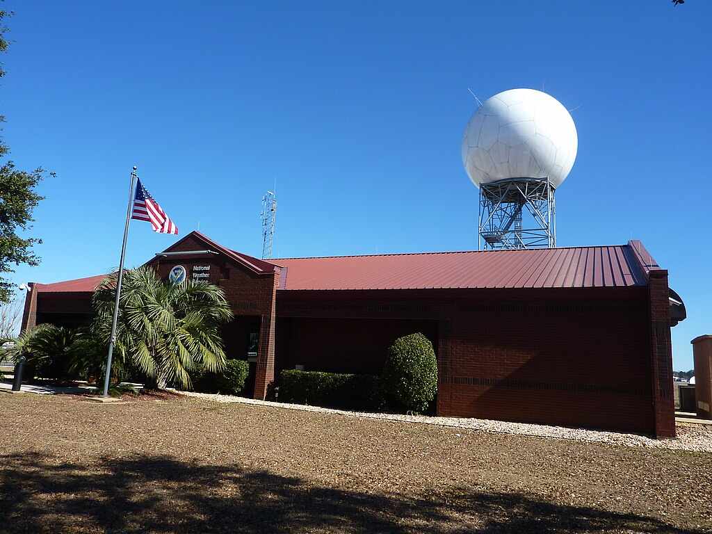 National Weather Service forecast office building with a NEXRAD Doppler radar dome at Mobile Regional Airport in Mobile, Alabama, under a clear blue sky.
