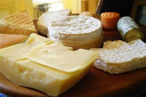 Representative Image. Assorted cheese varieties including white cheddar, soft-ripened cheese, and aged cheese arranged on wooden surface showing different textures and types susceptible to Listeria contamination