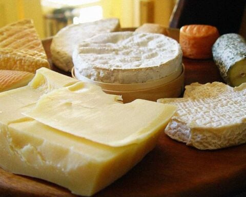 Representative Image. Assorted cheese varieties including white cheddar, soft-ripened cheese, and aged cheese arranged on wooden surface showing different textures and types susceptible to Listeria contamination