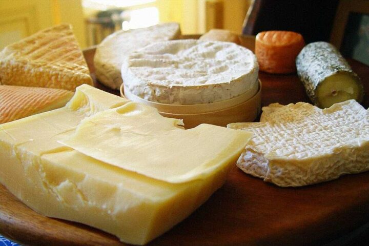 Representative Image. Assorted cheese varieties including white cheddar, soft-ripened cheese, and aged cheese arranged on wooden surface showing different textures and types susceptible to Listeria contamination