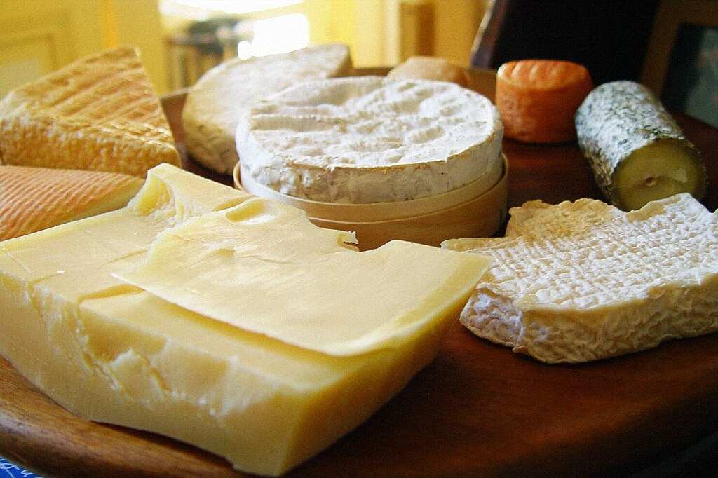Representative Image. Assorted cheese varieties including white cheddar, soft-ripened cheese, and aged cheese arranged on wooden surface showing different textures and types susceptible to Listeria contamination