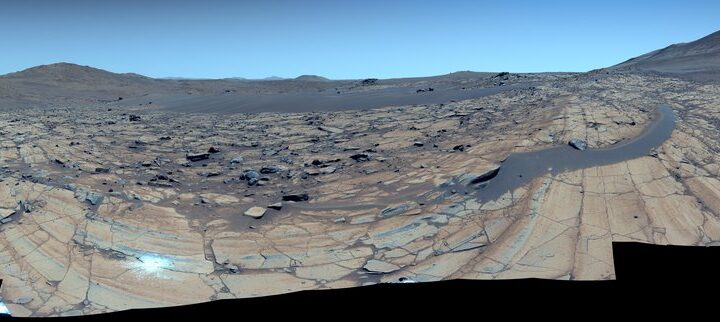 Enhanced-color 360° mosaic at ‘Falbreen’ showing fractured olivine-rich bedrock, distant hills, and a deceptively blue Martian sky.