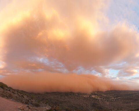 Massive orange-tinged dust storm (haboob) approaching Phoenix with a wall of dust illuminated by sunset, creating an apocalyptic scene as it envelops the metropolitan area.