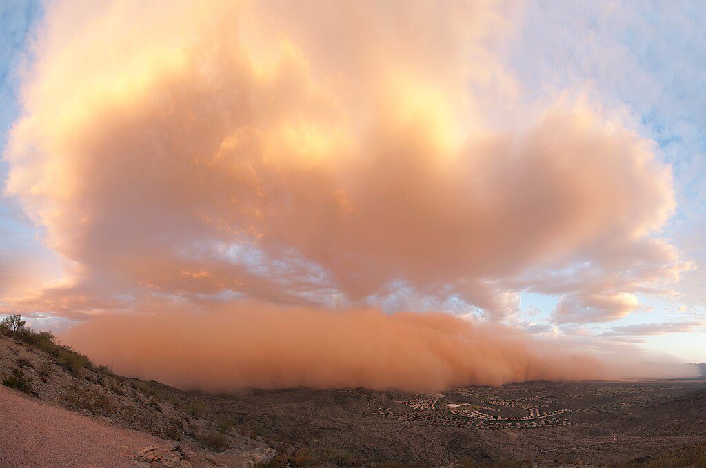 Massive orange-tinged dust storm (haboob) approaching Phoenix with a wall of dust illuminated by sunset, creating an apocalyptic scene as it envelops the metropolitan area.