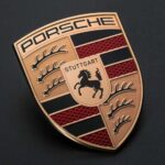 Porsche logo emblem with metallic gold finish on dark background representing the brand’s identity