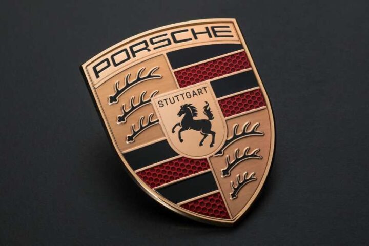 Porsche logo emblem with metallic gold finish on dark background representing the brand’s identity