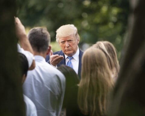 Donald J. Trump in a navy suit and bright blue tie pumps his fist while walking on an airport tarmac.