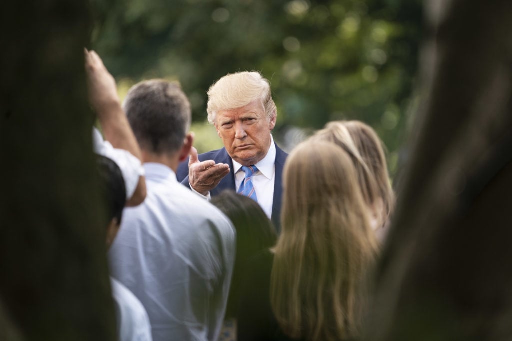 Donald J. Trump in a navy suit and bright blue tie pumps his fist while walking on an airport tarmac.