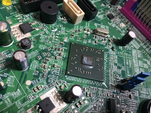 Close-up of a CPU chip mounted on a green printed circuit board, surrounded by capacitors and connectors.