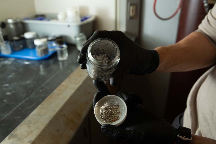 Researcher holding jar of recycled aluminum pellets used in MIT's sustainable hydrogen production process, showcasing the raw materials for clean energy generation.