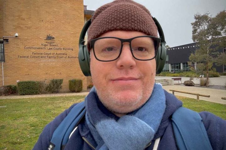 Richard Boyle wearing a beanie, glasses, and headphones, standing outside the Federal Court of Australia in Canberra.