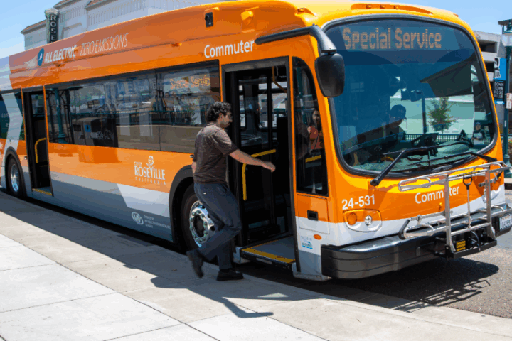 Orange all-electric Roseville Commuter bus with ‘Special Service’ on the display, with a rider boarding.