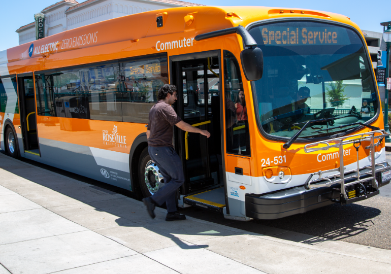 Orange all-electric Roseville Commuter bus with ‘Special Service’ on the display, with a rider boarding.