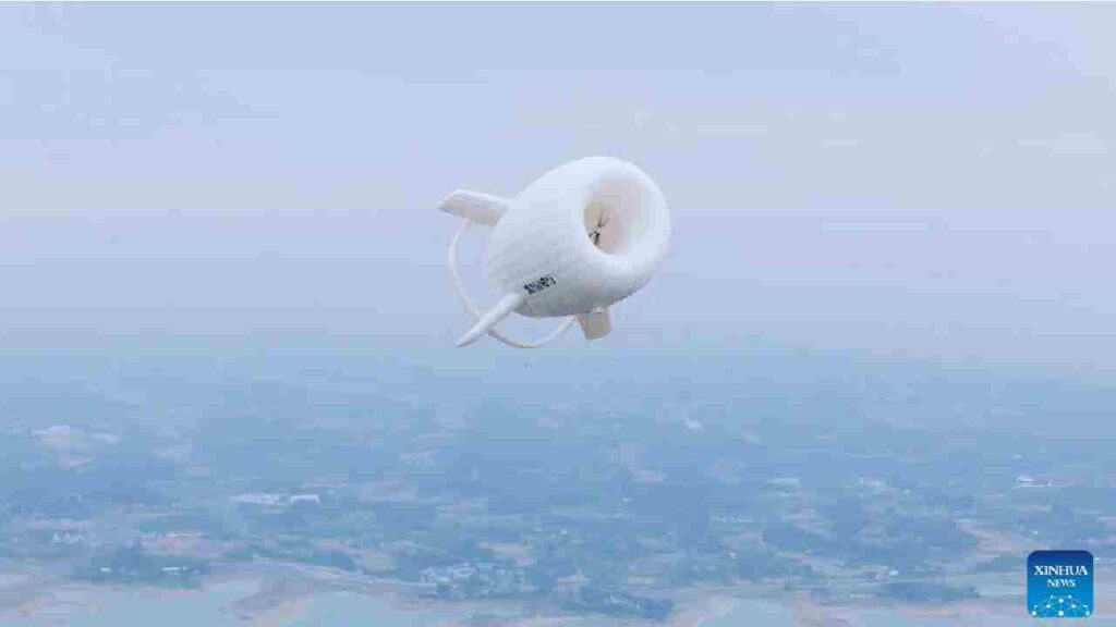 White torus‑shaped airborne wind turbine with stabilizing fins flying over mixed land and water landscape, branded “XUWEI,” credited to Xinhua News.