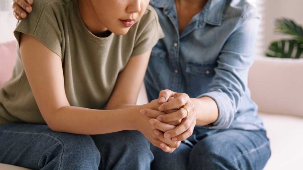 Person receiving emotional support from another individual, with their hands clasped together in a moment of connection, representing therapeutic relationships that benefit sensitive individuals.