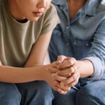 Person receiving emotional support from another individual, with their hands clasped together in a moment of connection, representing therapeutic relationships that benefit sensitive individuals.