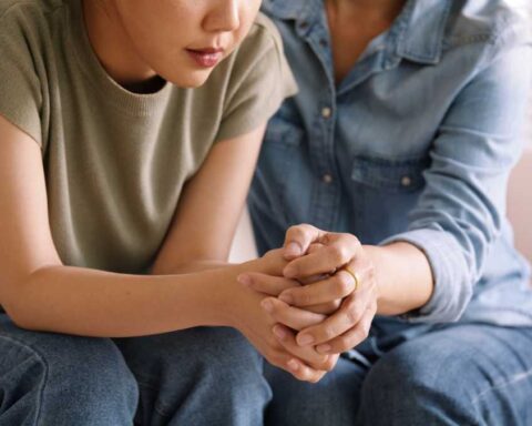 Person receiving emotional support from another individual, with their hands clasped together in a moment of connection, representing therapeutic relationships that benefit sensitive individuals.